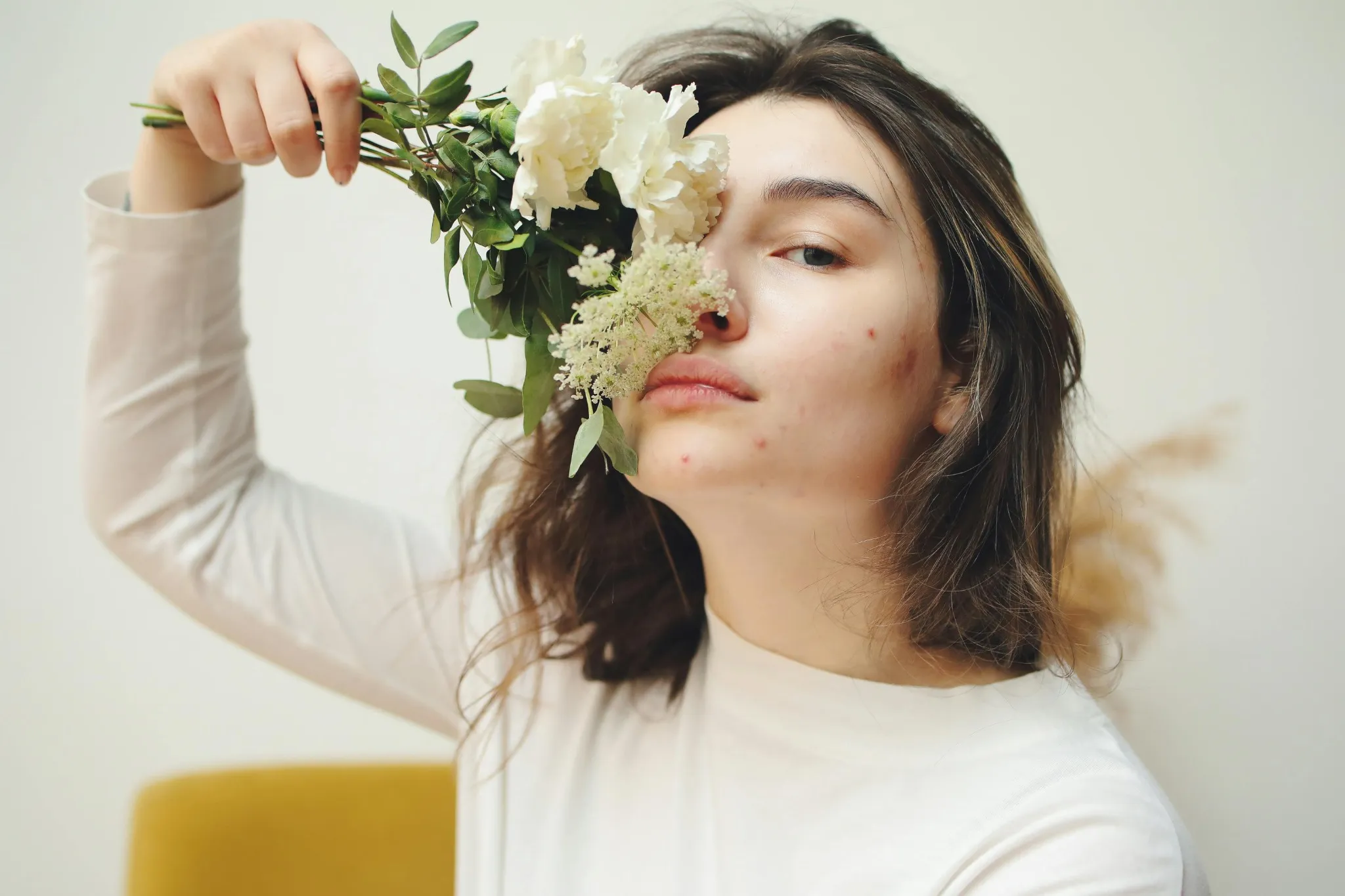 A woman with pimples and acne scars partially covering her face with a flower | Shine Dermatology